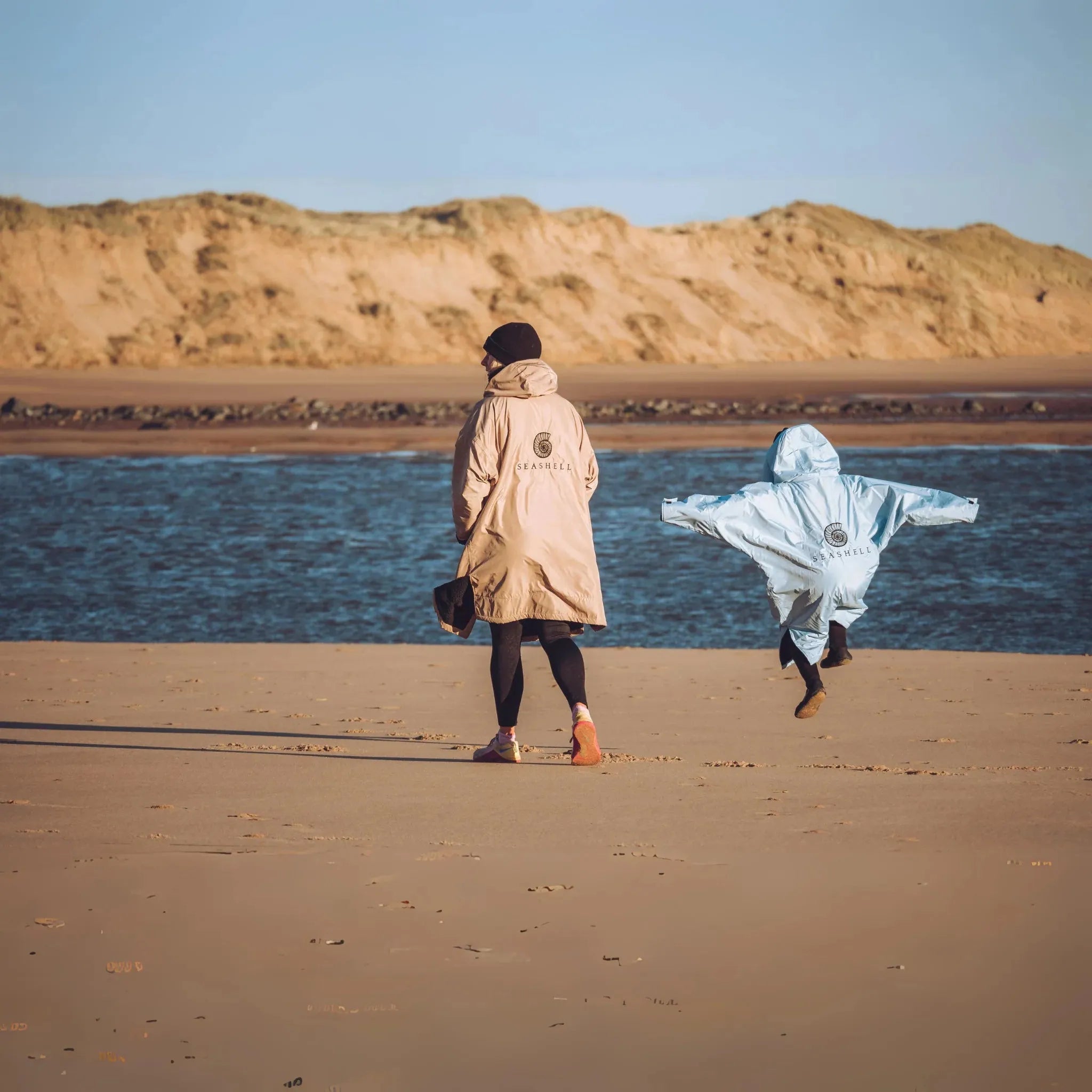 A woman and child on the beach wearing their Seashell changing robes in the colours ocean and sand