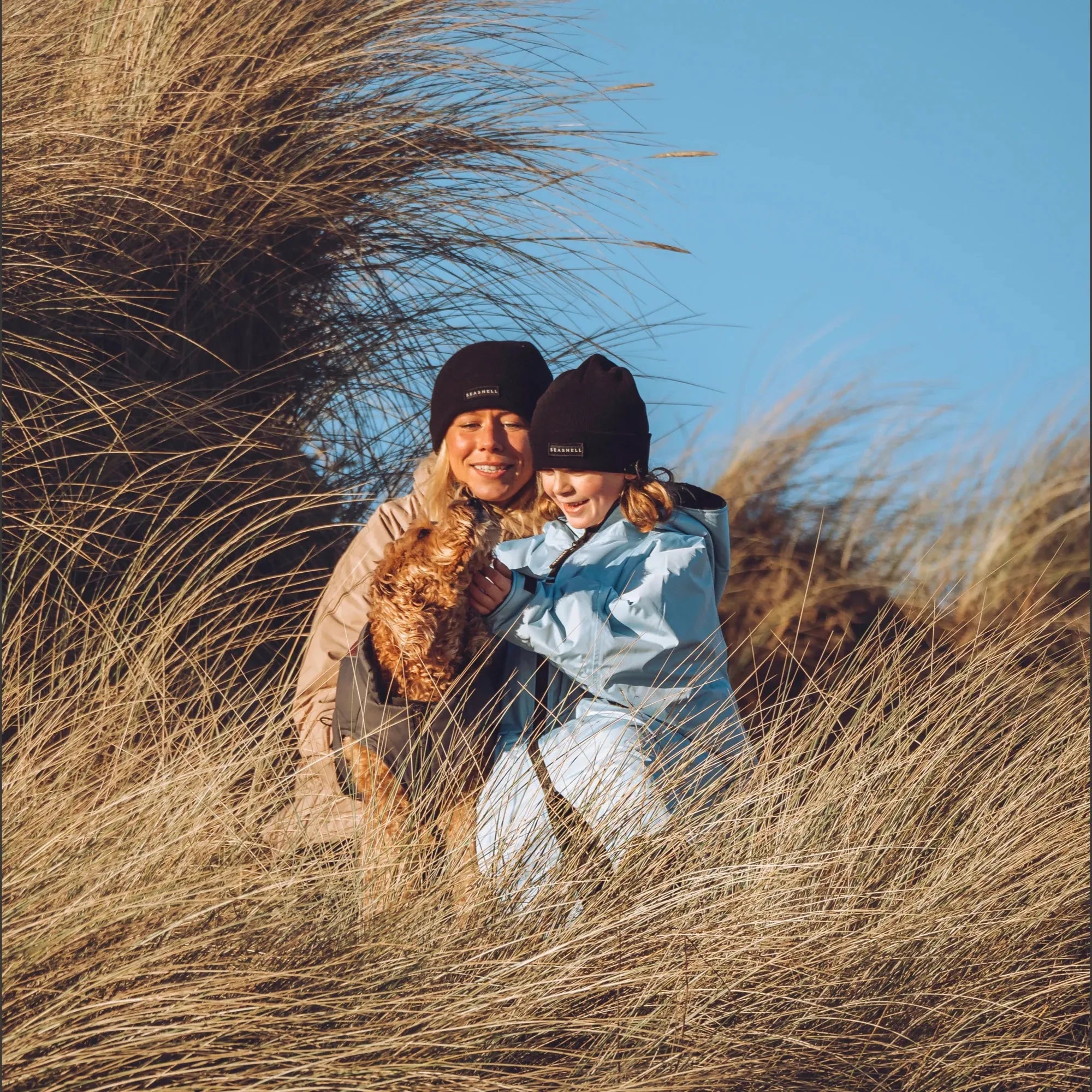 A woman and child on the beach wearing their Seashell changing robes in the colours ocean and sand