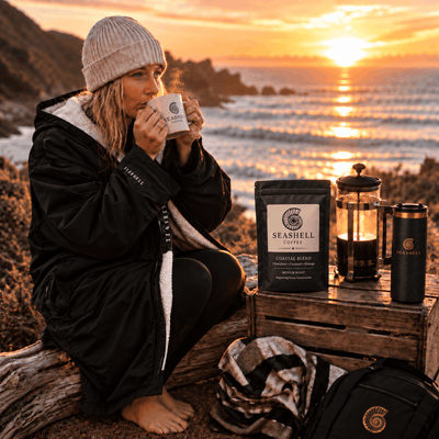 Swimmer in a Seashell changing robe drinking coffee at sunrise on the coast