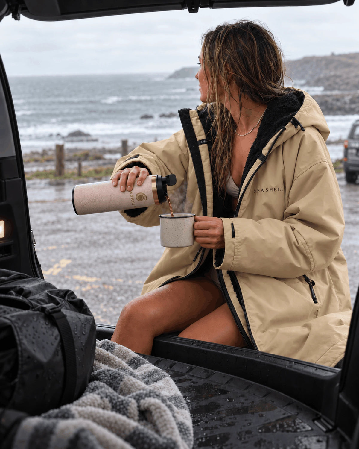 Swimmer in a Sand Seashell changing robe pouring coffee from the Sand Flip Top Flask in the car boot